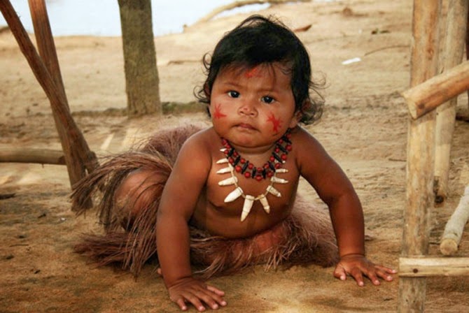 Criança indígena com roupa de palha e adorno de sementes, em uma área em desertificação